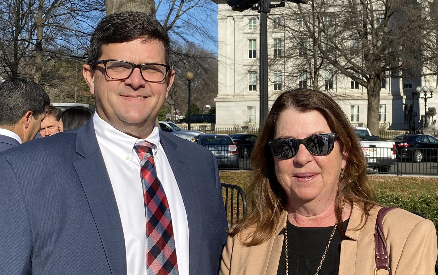 Man and woman dressed in business clothes stand outside in White House security line