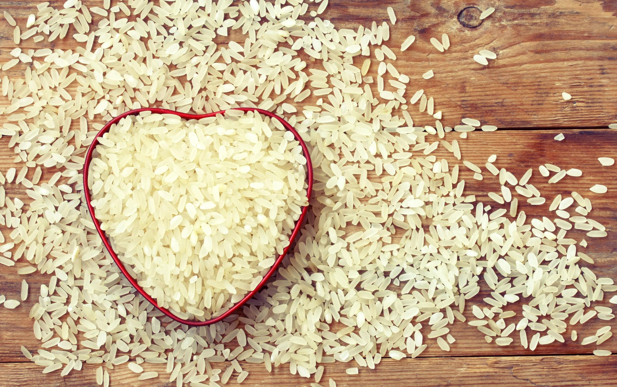 White rice inside red heart shape spilling onto wooden plank