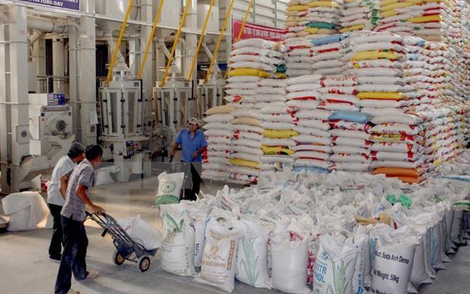 Rice bags stacked to ceiling in warehouse, workers transport more bags using dolly