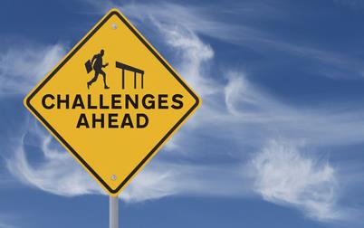 Yellow street sign with text "Challenges ahead" and silouhette of man carrying briefcase getting ready to leap over a hurdle 