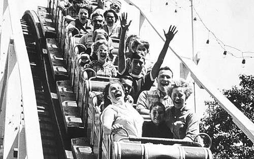 B/W photo of people riding on a wooden roller coaster