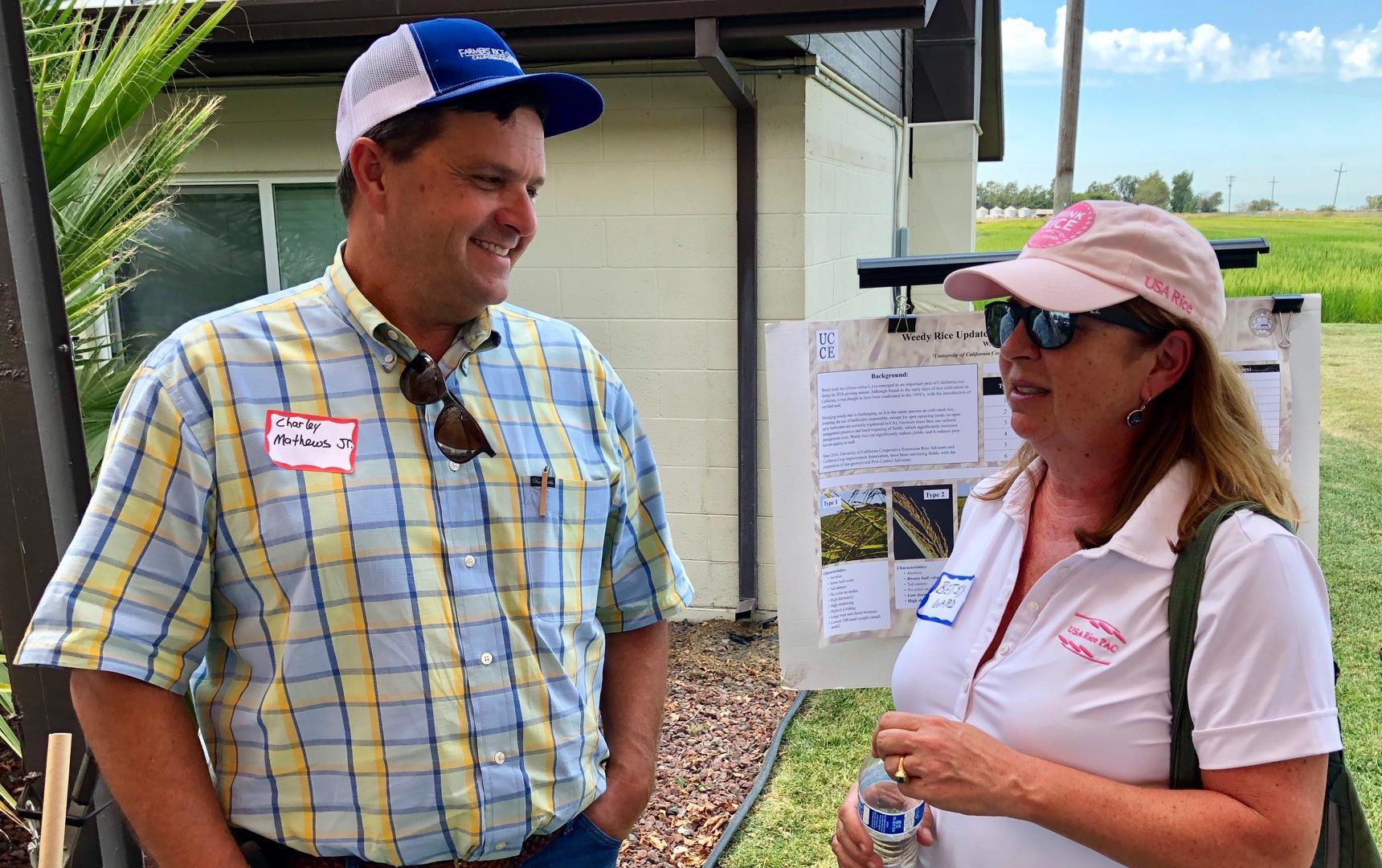 Man in yellow and blue plaid shirt talks with woman wearing pink shirt & hat