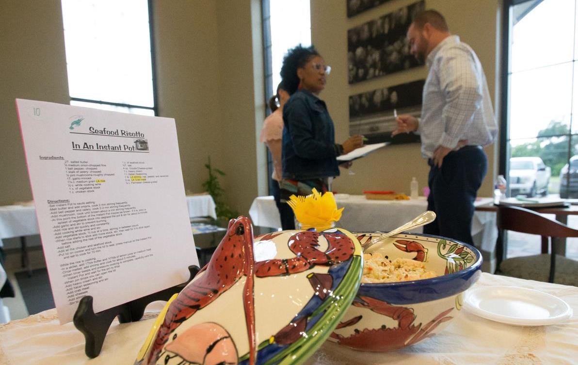 Foreground shows rice served in baking dish decorated with red crawfish, recipe card on easel, background shows several people standing at another table, Rick Hickman photo