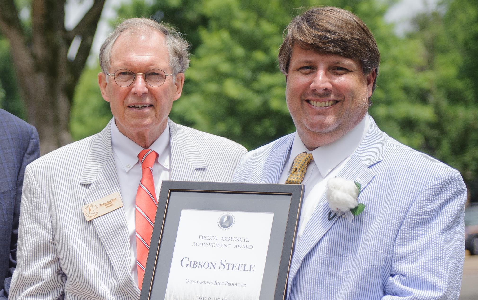 Two white men wearing seersucker suits holding a plaque for Rice Farmer of the Year