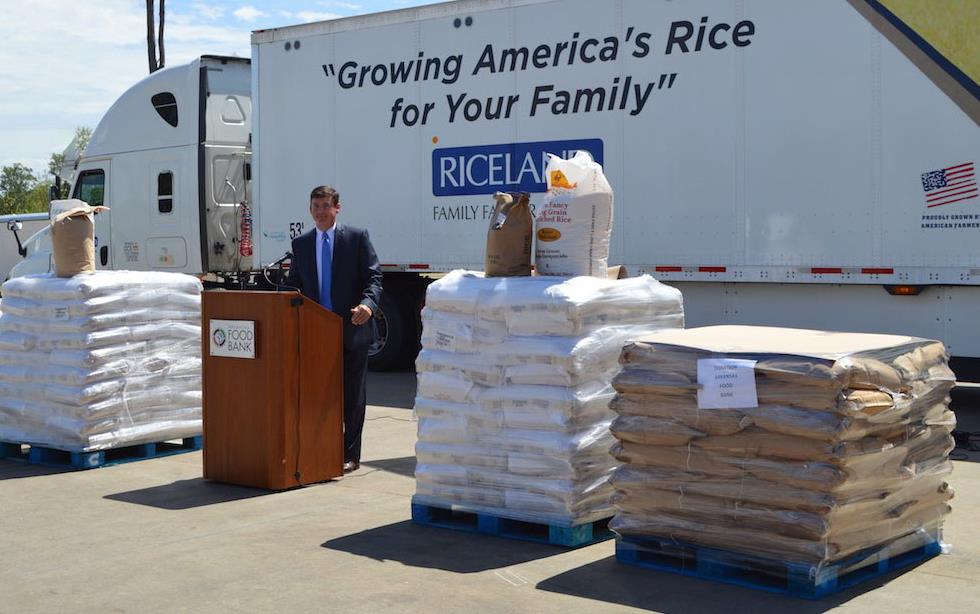 AR Foodbank Donation, Jeff Rutledge stands in front of podium, large bags of rice on pallets and semi-truck in background
