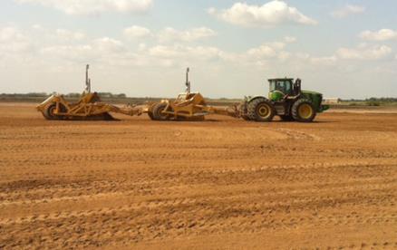 Green tractor pulls two land levelers across brown dirt field