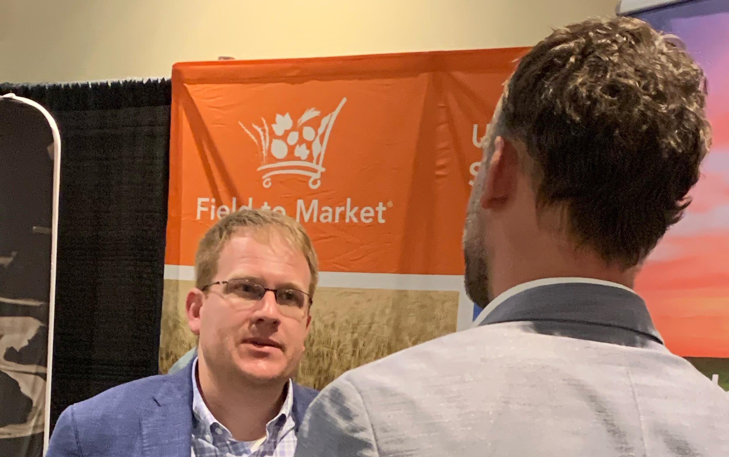 Two men stand in front of orange banner that reads: Field to Market