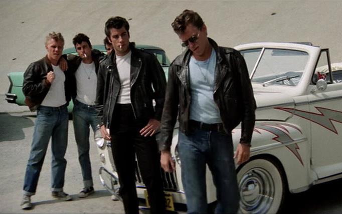  From the movie "Grease," boy gang in leather jackets, girl gang in pink jackets stand around souped up roadster