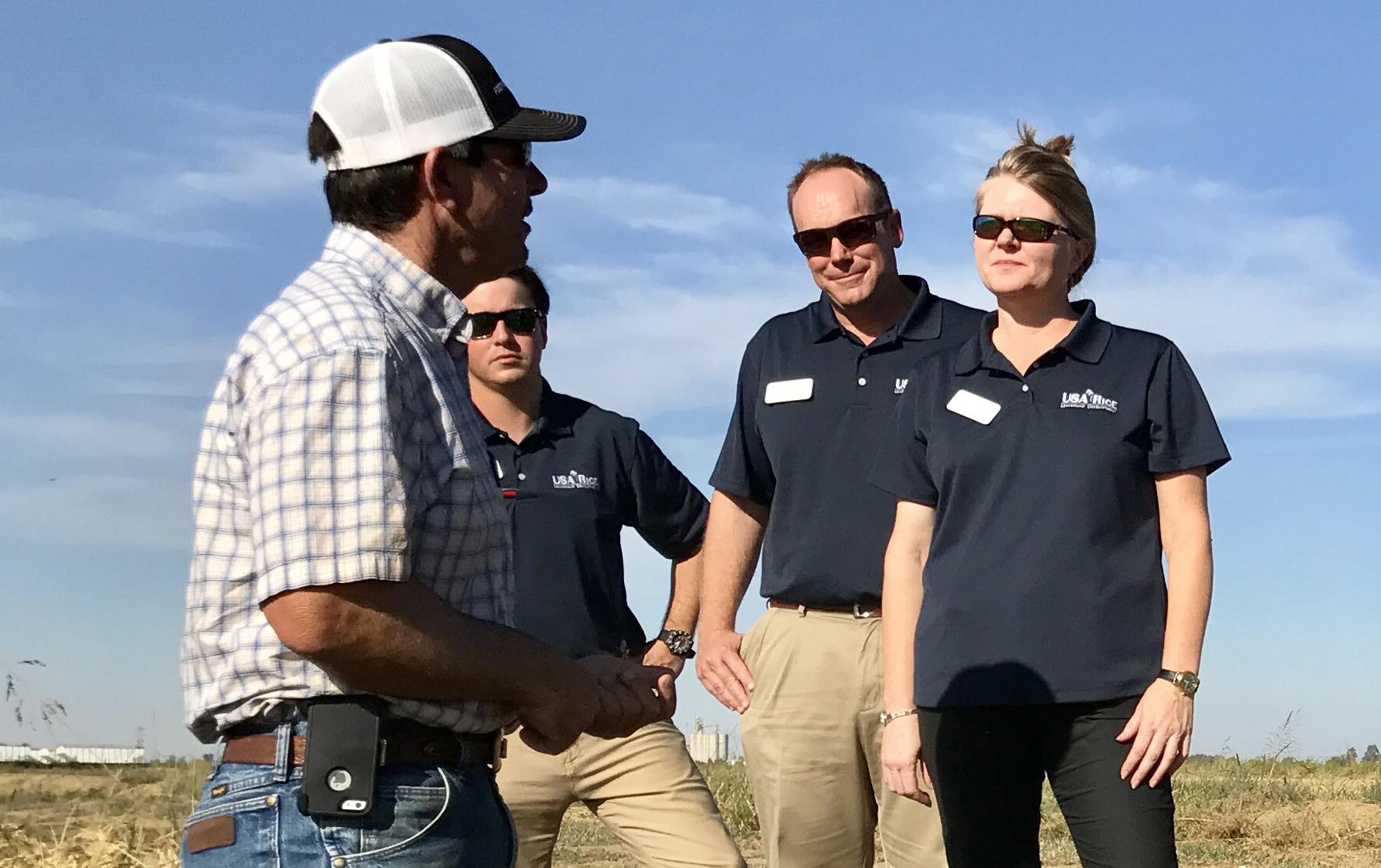 Group standing in a rice field, listening to farmer, everyone wearing sunglasses