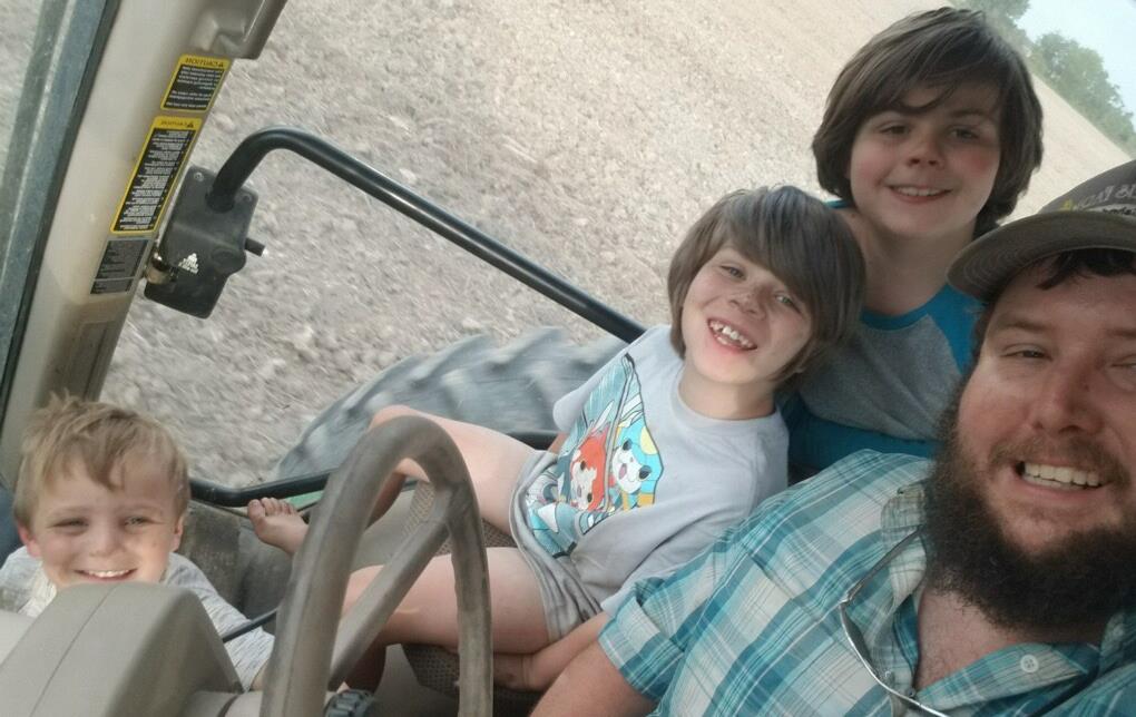 Farmer in combine cab surrounded by three young boys