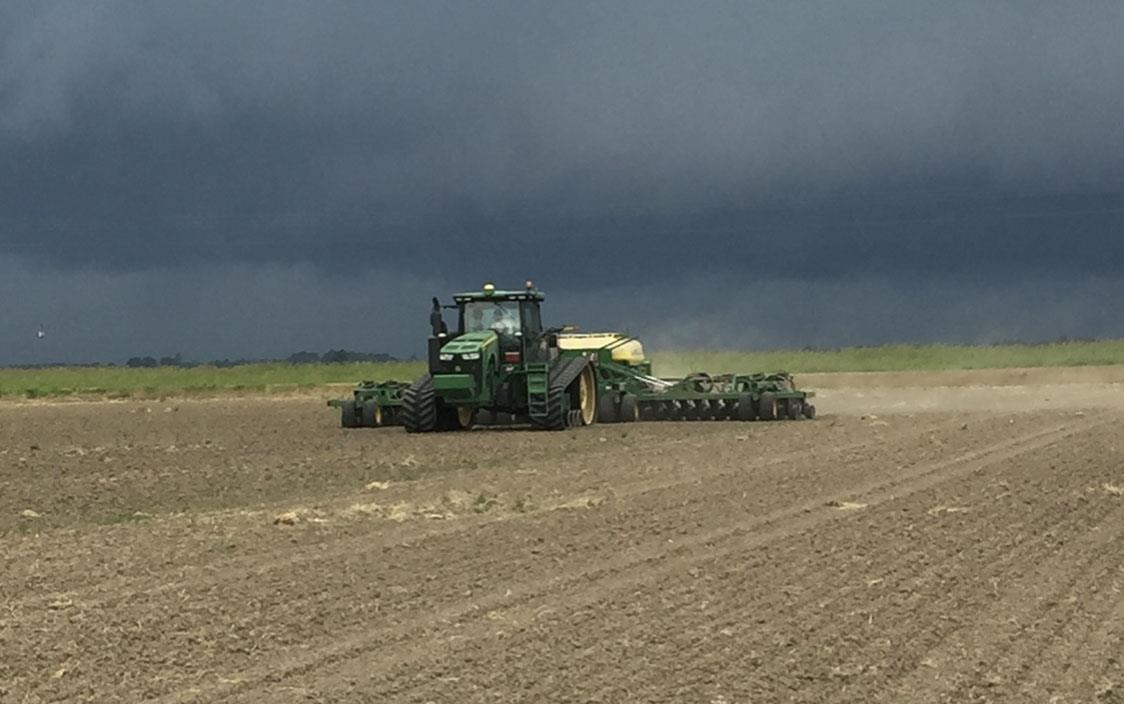 Green combine planting in dirt field, ominous dark storm clouds overhead