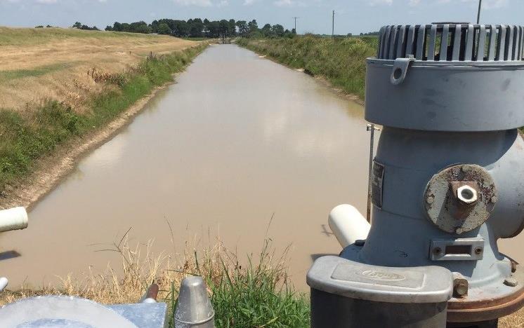 Re-Lift pump on irrigation canal in foreground, canal stretches out to grove of trees in background