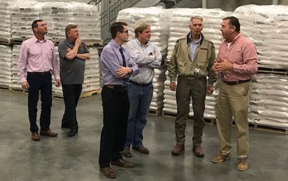 Group of men stand in warehouse filled with white rice bags stacked on pallets